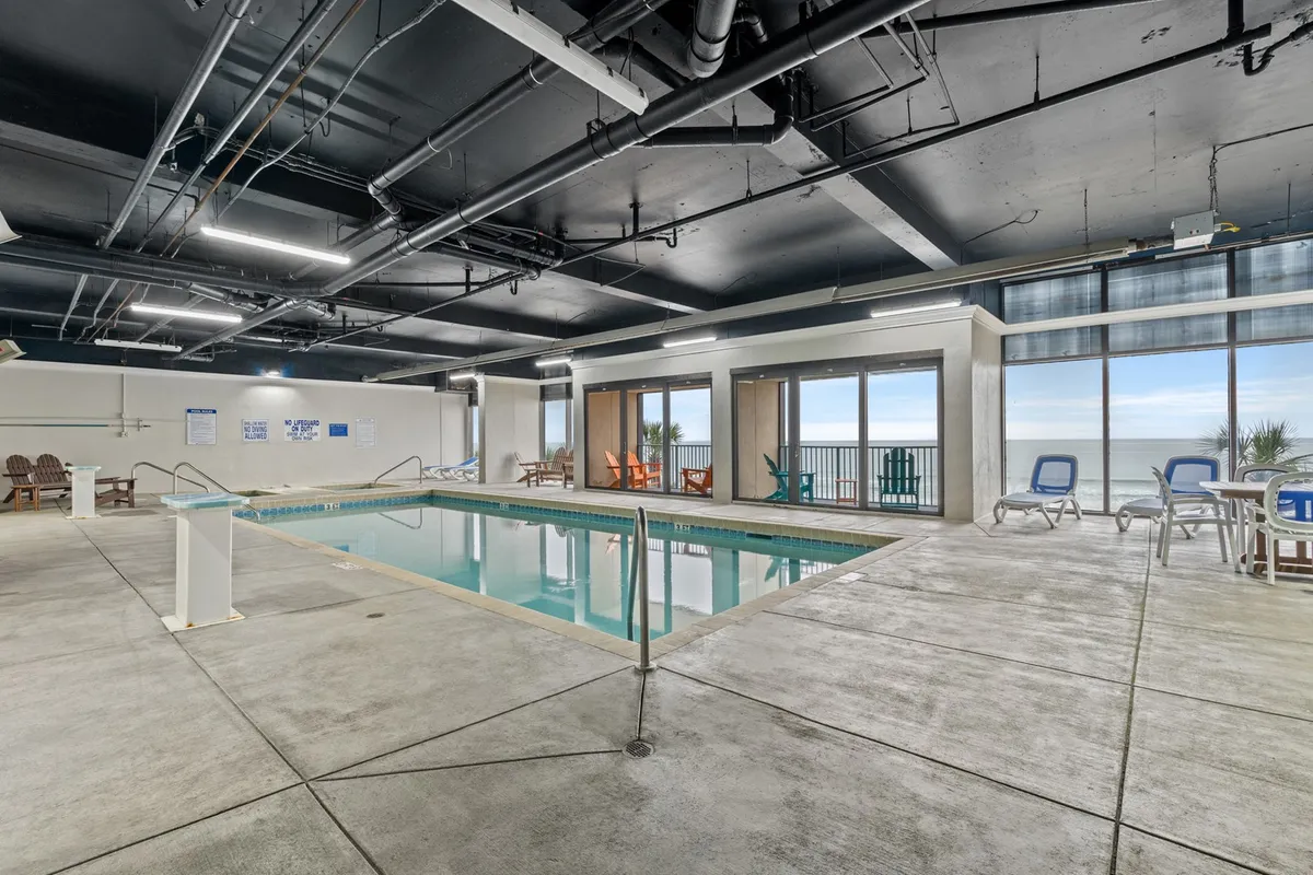 This interior shot features a spacious indoor swimming pool area with large windows offering ocean views and colorful lounge chairs arranged around the pool, creating a tranquil and inviting atmosphere.