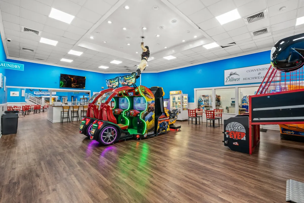 This image captures a vibrant arcade area with bold colors and a suspended figure, where guests are seen playing games, socializing, and enjoying themselves. The playful ambiance highlights the joy and camaraderie of shared experiences.