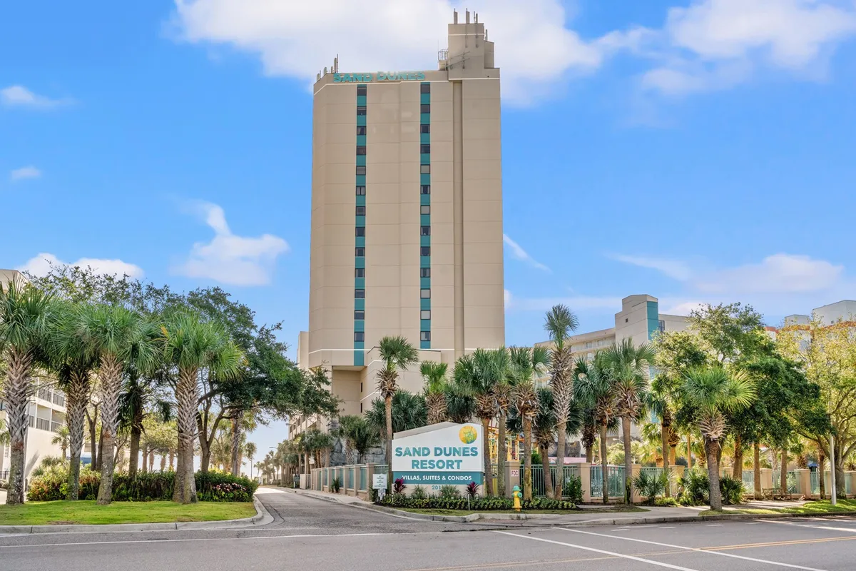 This image displays the tall resort building surrounded by palm trees, with a welcoming sign visible. The scene is bathed in inviting sunlight and hints at the resort’s proximity to the beach, as well as the outdoor amenities guests can enjoy, such as pools and beachfront activities.