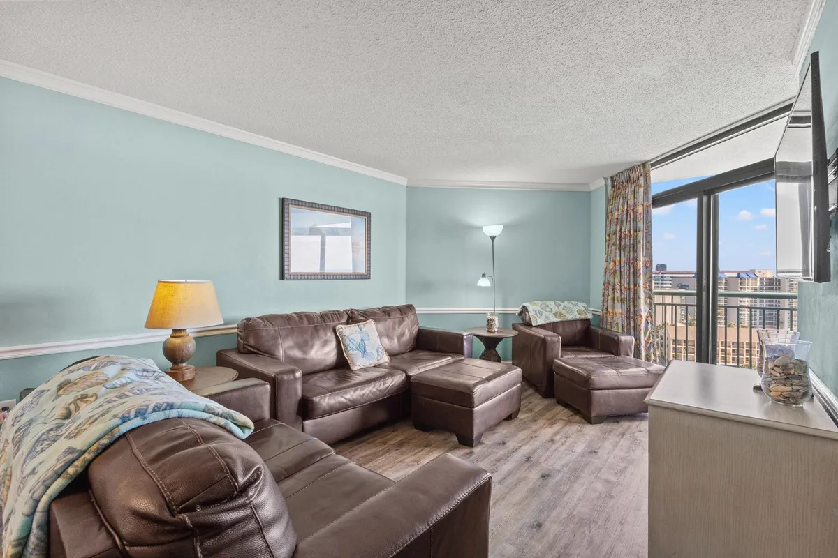 This cozy living room features plush brown leather sofas adorned with decorative throw pillows, all centered around expansive floor-to-ceiling windows that fill the space with natural light and reveal breathtaking ocean views. The inviting setup creates the perfect atmosphere for relaxing, socializing, or enjoying a movie night with friends and family.