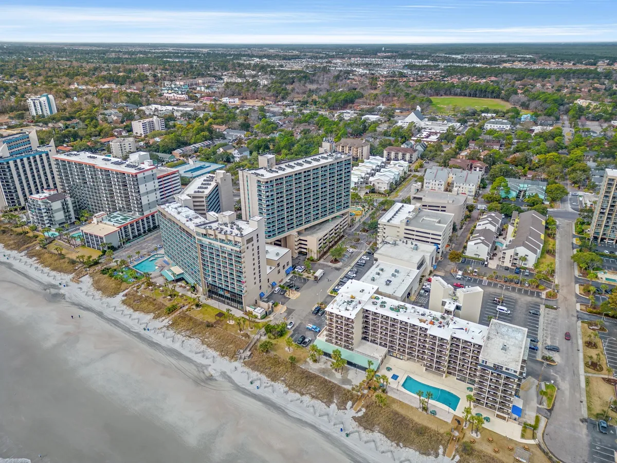 A vibrant panoramic exterior view showcasing beachfront hotels, multiple swimming pools, and the lively beachfront atmosphere. The image captures people swimming, sunbathing, and walking along the beach, with the hotels and ocean as a dynamic backdrop.